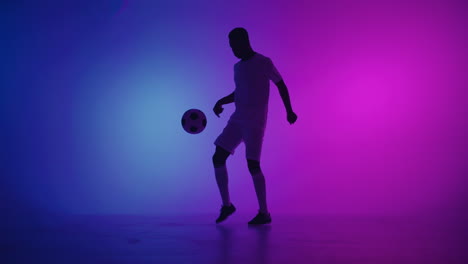 Black-man-a-player-juggles-football-ball-in-a-dark-studio-with-neon-lights-on-the-floor-and-red-and-blue-lighting-effects-in-slow-motion.-African-professional-football-soccer-player